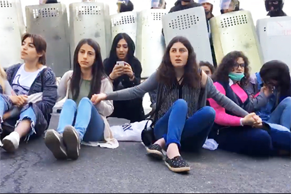 Young women stage a sit-in in front of riot police, which on Monday attacked protesters