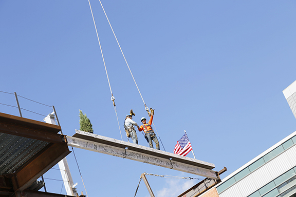 Beam is being listed to be hoisted with a tree, also adorned with the American flag